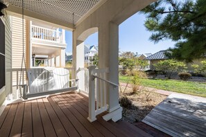 A covered porch with a swing chair, a white railing, and a view of a residential area. - Sunset Island 5 Beachside Mews (Ocean City)