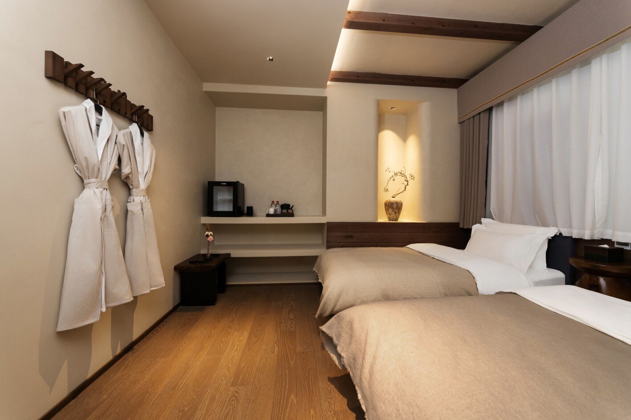 Une chambre d’hôtel avec deux lits, une télévision, une petite table et une étagère avec des articles de toilette.