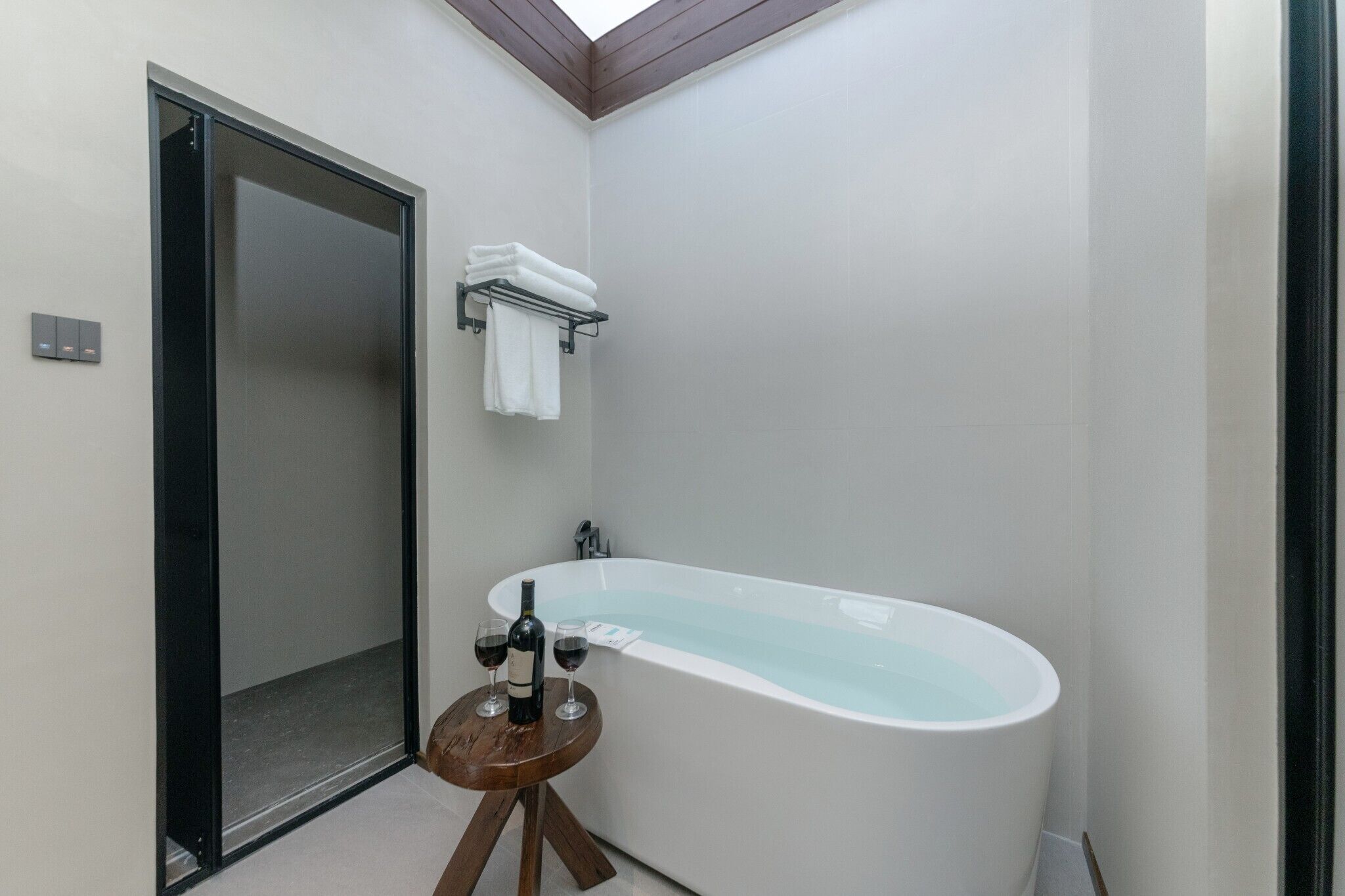 Een moderne badkamer met een vrijstaand bad, een houten kruk en een handdoekhouder.