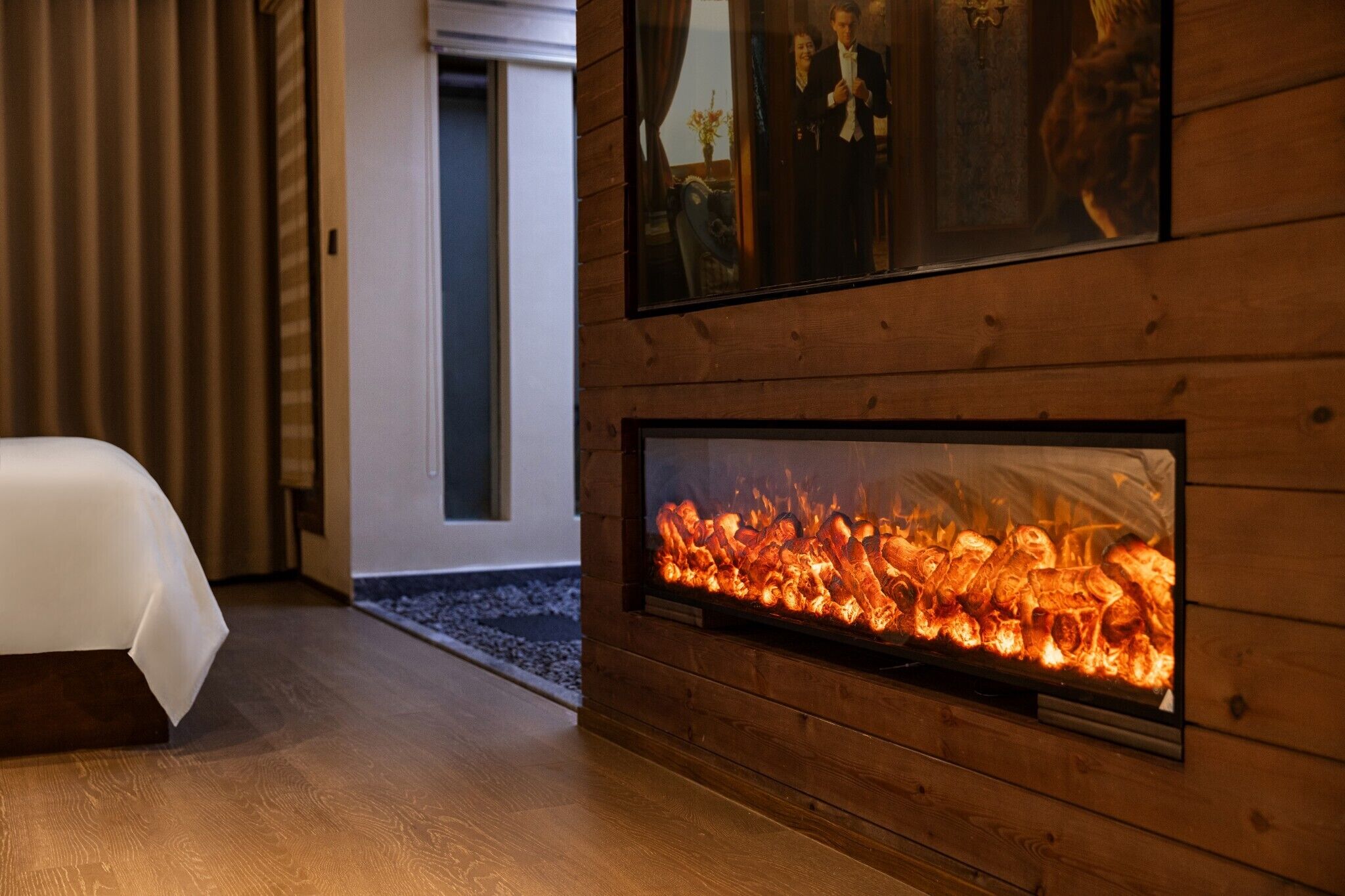 A room with a bed, a fireplace, wooden paneling, and a framed picture on the wall.