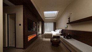 A hotel room with a bed, a TV mounted on the wall, a fireplace, a skylight, and a bedside table. - Shangri-La Homestay Designer B&B (Deqin)