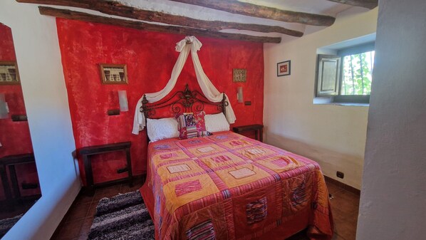 Ein Schlafzimmer mit einem Himmelbett, einer roten Wand und einem Fenster mit Blick auf Grünflächen.