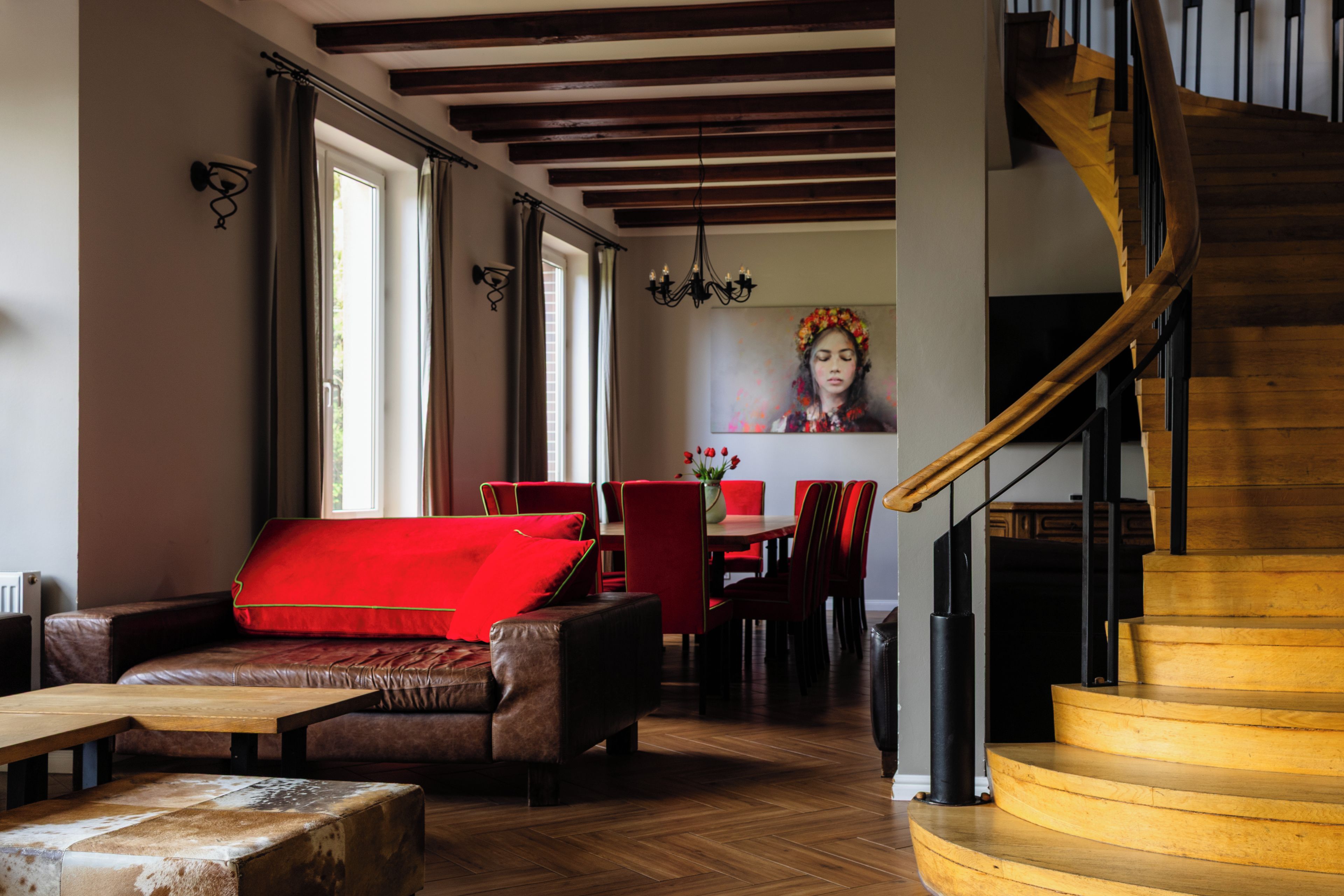 Un interior moderno con escalera de madera, mobiliario de cuero y zona de comedor con sillas rojas.