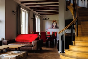 A modern interior with a wooden staircase, leather furniture, and a dining area with red chairs.