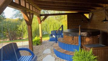 Un espacio al aire libre techado con un jacuzzi, asientos de madera y un camino de piedra.