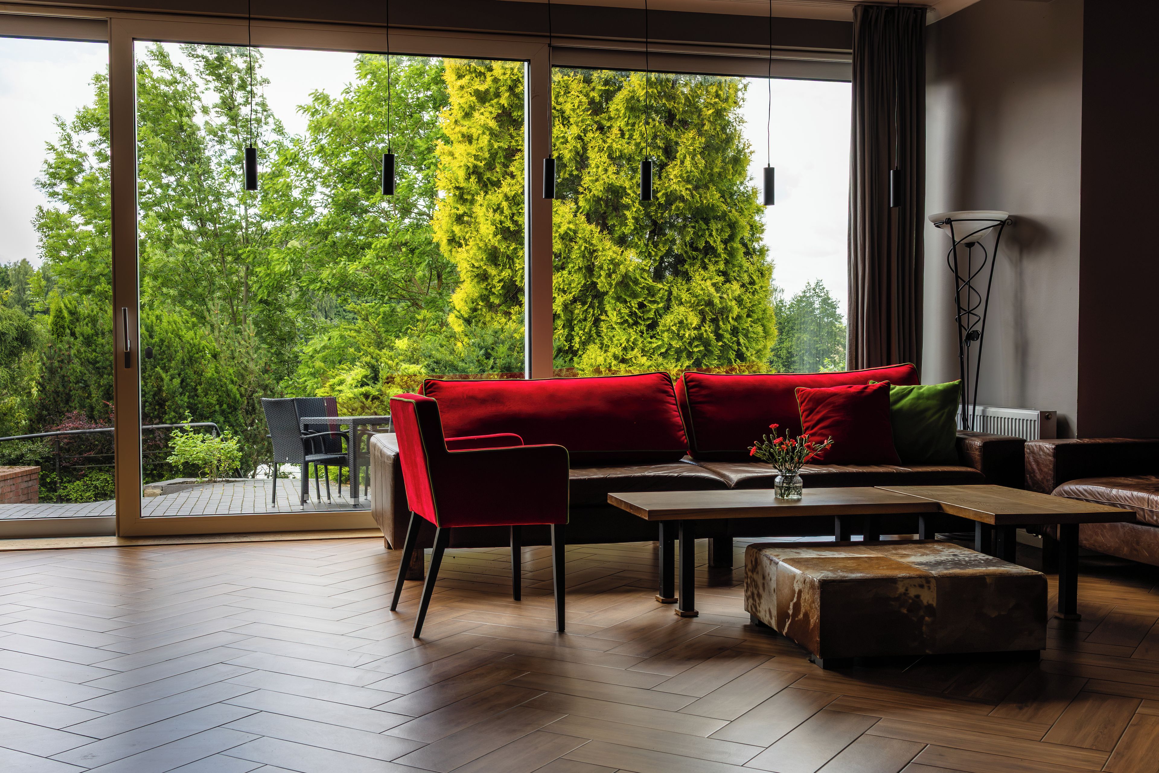 Una sala moderna con un sofá rojo, una mesa de centro de madera y vistas a un exuberante follaje a través de amplios ventanales.