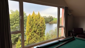 Een pooltafel in een ruimte met grote ramen met uitzicht op een meer en bomen.