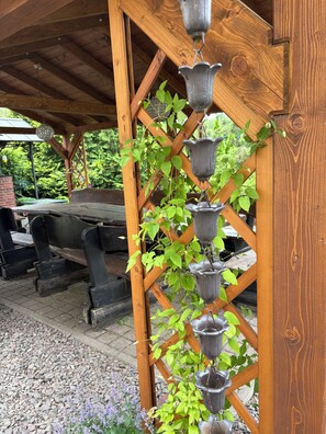 A wooden pergola with a climbing plant and hanging metal containers. - Property for 22 guests, private lake, tennis court, sauna, hot tub, no neighbors (Zblewo)