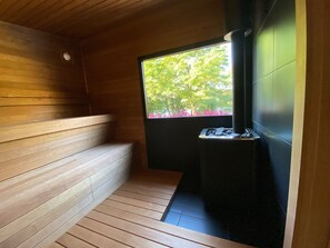 Un sauna avec des bancs en bois et une fenêtre donnant sur des arbres et des fleurs roses.