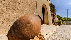 A large, rusted pot in front of a building with an arched doorway and a stone wall. - Villa Moli dén Llull (Sant Llorenç Des Cardassar)