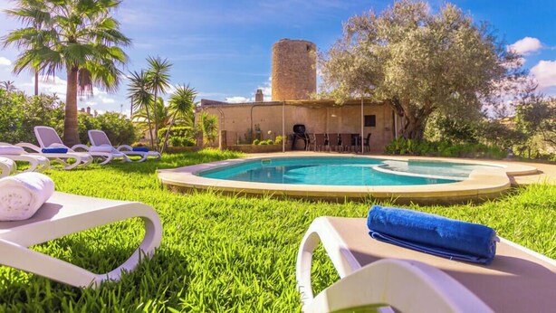 A pool area with lounge chairs, a stone tower, and lush greenery. - Villa Moli dén Llull (Sant Llorenç Des Cardassar)