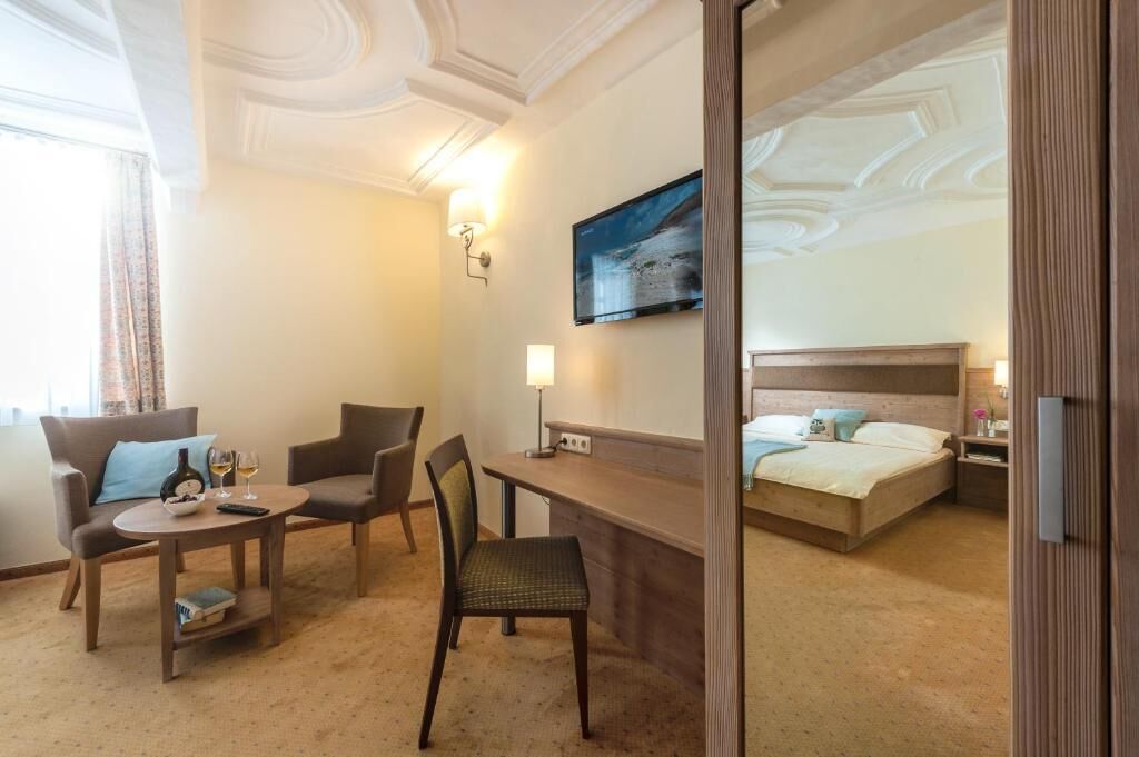 A hotel room with a bed, a desk with a chair, a sofa, and a TV mounted on the wall.