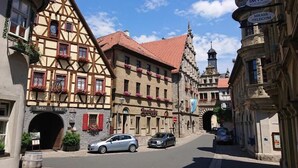 Eine Straße mit traditionellen Fachwerkhäusern, einem gut sichtbaren Hotel Eingang und blauem Himmel.