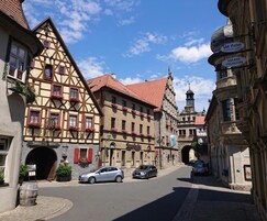 Rua com edifícios tradicionais de enxaimel, entrada de hotel visível e céu claro.