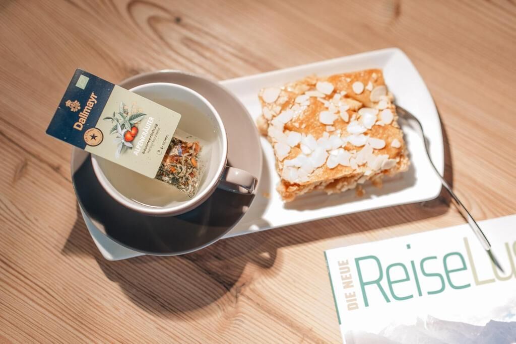 A cup of tea with a tea bag and a slice of almond cake on a white plate.