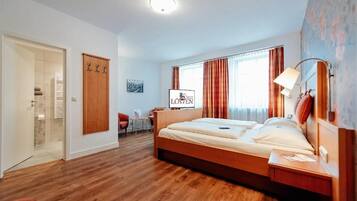A hotel room with a wooden bed, a desk, a chair, a wardrobe, and a bathroom visible through an open door.
