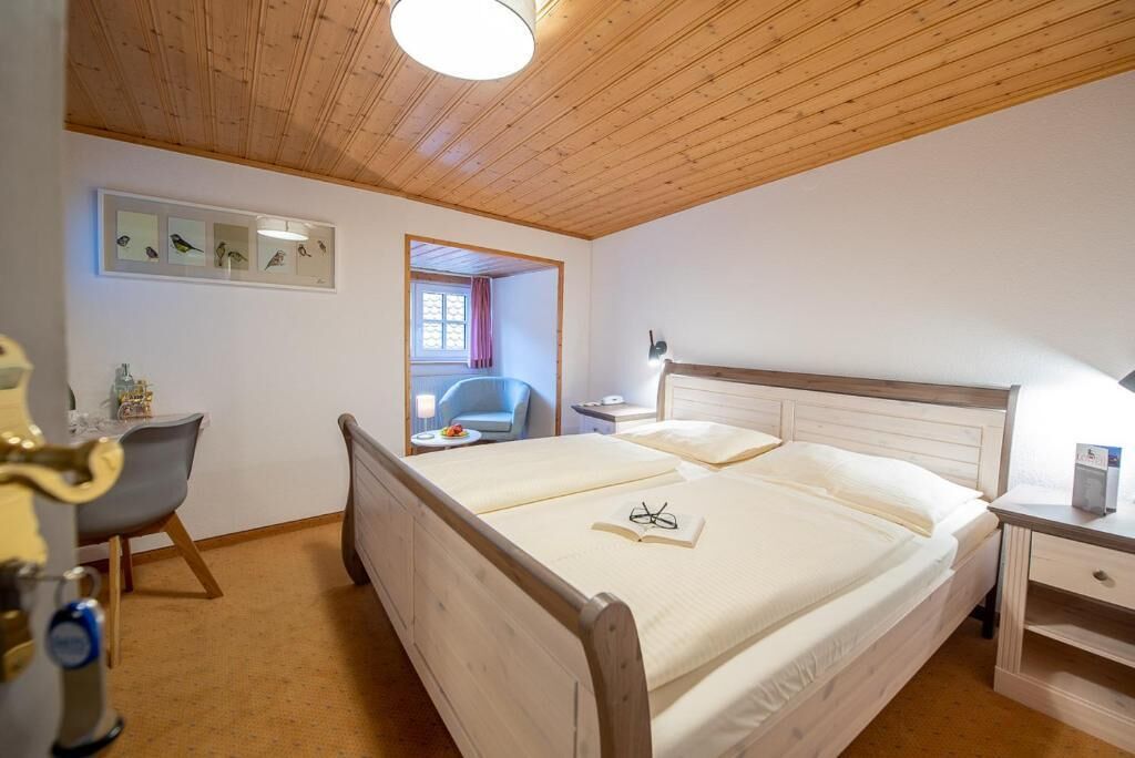 Une chambre avec un lit en bois, un bureau et une chaise. Il y a une fenêtre donnant sur l’extérieur.