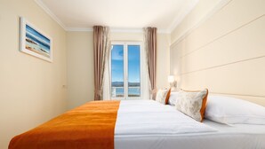 Camera d'albergo con un letto grande, pareti color beige, un quadro appeso e vista sul mare dalla finestra.