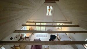 A high-ceilinged attic room with a large window, a sofa, a chair, and a dining table. - Charming holiday home in beautiful Österlen |SE01085 (Gärsnäs)