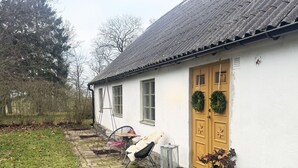 A white house with a wooden door, two windows, and a small porch with a chair and a table. - Charming holiday home in beautiful Österlen |SE01085 (Gärsnäs)