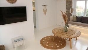 A modern living room with a flat-screen TV, a round wooden table with a woven placemat, a small stool, and a woven rug. - Villa Adelfia with private hot tub (Mykonos)