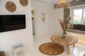 A modern living room with a flat-screen TV, a round wooden table with a woven placemat, a small stool, and a woven rug. - Villa Adelfia with private hot tub (Mykonos)