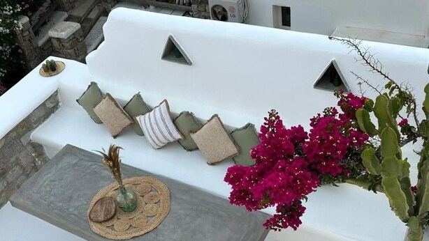 A white outdoor seating area with a stone table, cushions, and a vase of flowers. - Villa Adelfia with private hot tub (Mykonos)