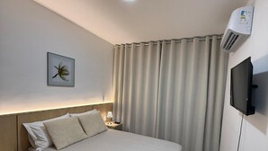 Ein Hotelzimmer mit Bett, Nachttisch, Lampe, Klimaanlage und an der Wand montiertem Fernseher.