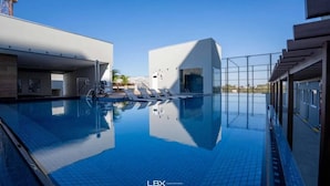 Ein moderner Poolbereich mit klarem, blauen Wasser, einer Sonnensegelkonstruktion und Blick auf die umliegenden Gebäude.