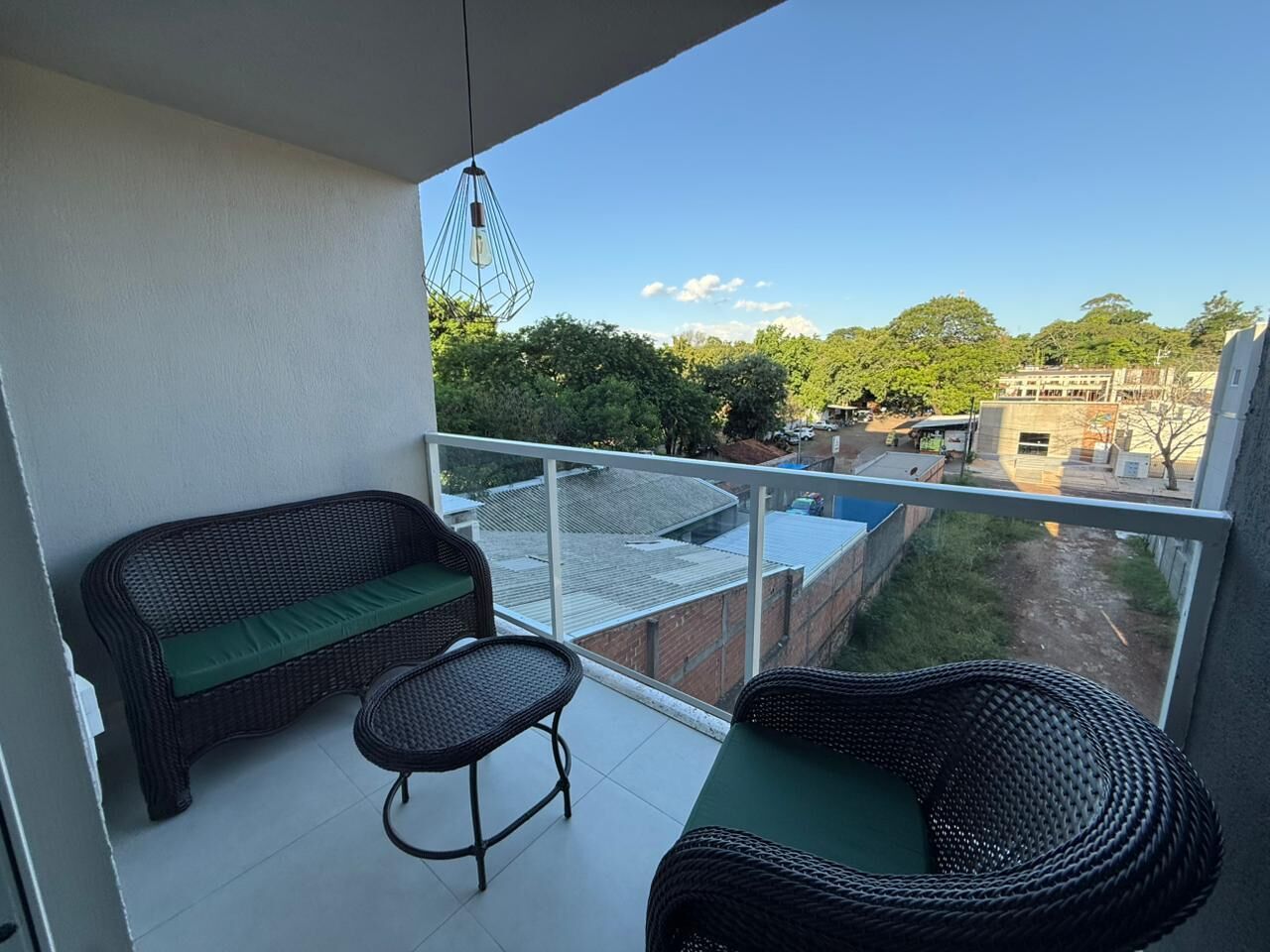En balkon med fletmøbler, udsigt til en bygning og en klar himmel.