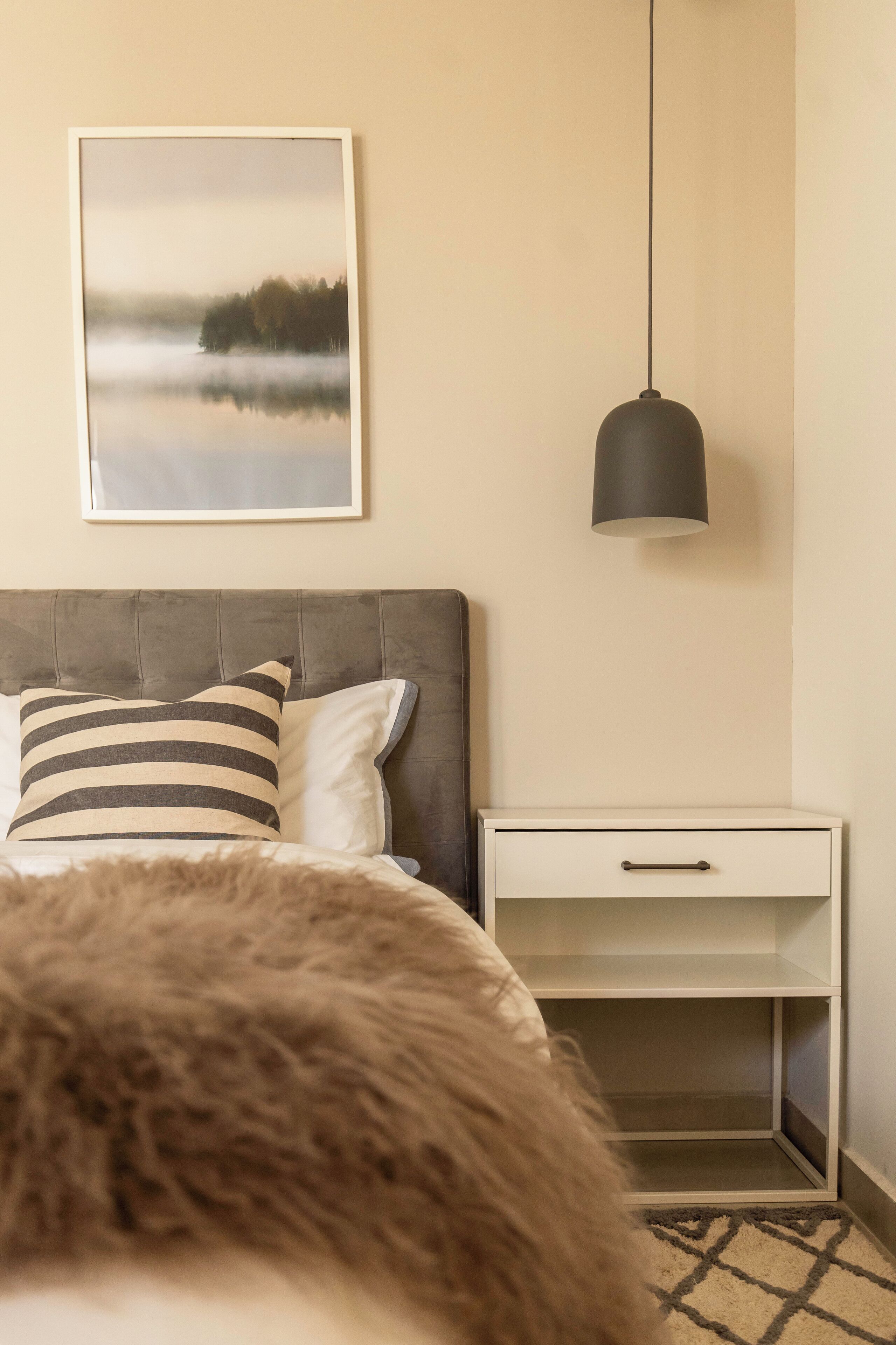 Une chambre à coucher avec un lit, une table de chevet, un tableau encadré et une lampe suspendue.