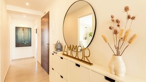 A hallway with a wooden door, a white console table with a mirror, a vase with dried plants, and a framed artwork on the wall. - Modern & Spacious 3BD Apt With Terrace (Msida)