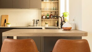 A modern kitchen with a central island, two brown leather bar stools, and wooden cabinets. - Modern & Spacious 3BD Apt With Terrace (Msida)