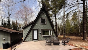 A cabin with a deck, a small porch, and a window. - Northern MI Secluded A-Frame Cabin: ORVs, Fish/Hunt, Projector, Golf, EV, Pool (Grayling)