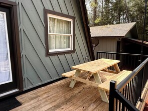 A wooden deck with a picnic table and a window. - Northern MI Secluded A-Frame Cabin: ORVs, Fish/Hunt, Projector, Golf, EV, Pool (Grayling)