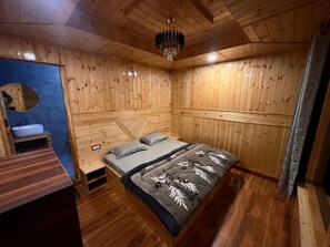 A wooden room with a bed, a small table, and a mirror.