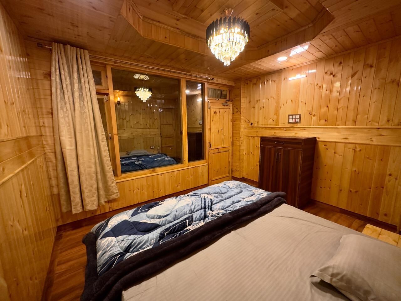 A wooden-paneled room with a bed, a chandelier, and a window with curtains.