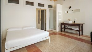 Une chambre à coucher avec un lit, un plafond en bois, une salle de bain avec un lavabo et un miroir, et une porte donnant sur une autre pièce.