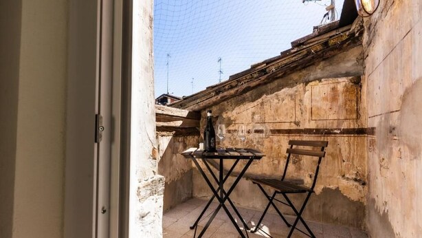 Une petite terrasse extérieure avec une table et une chaise, un sol en béton et un mur dont l’aspect a été altéré par les intempéries.