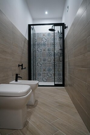Un baño moderno con zona de ducha, dos inodoros y un salpicadero de azulejos estampados.