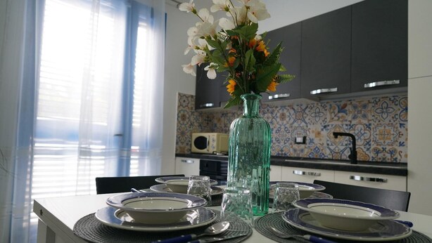 A dining table set with plates, glasses, and cutlery in a modern kitchen with patterned tiles and a vase of flowers. - Apartment   Ground Floor (balestrate)