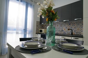 Una mesa de comedor dispuesta con platos, vasos y cubiertos en una cocina moderna con baldosas estampadas y un jarrón de flores.