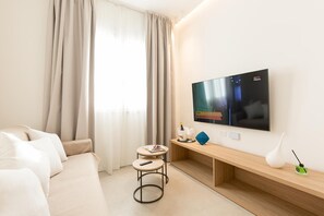 A modern hotel room with a large flat-screen TV mounted on the wall, a sofa, a small round table with a remote control, a wooden console table with a decorative item, and a window with sheer curtains. - Appartamento Luxury  Cristallo Terrasini (Terrasini)