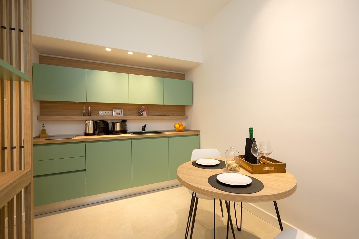 A modern kitchen with green cabinets, a wooden countertop, and a dining area with a round table.