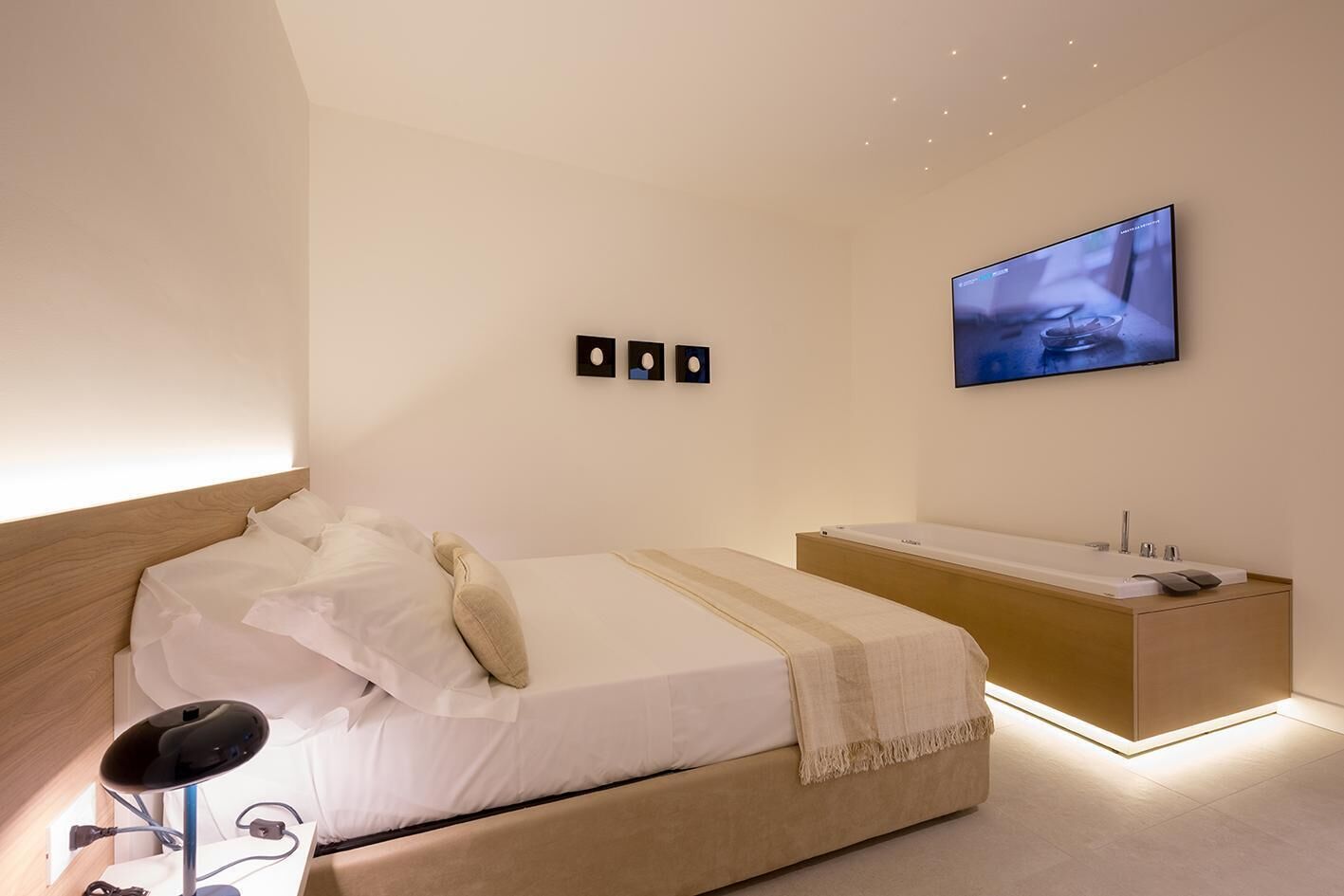 Una camera da letto moderna con un letto, un comodino e una TV a parete.