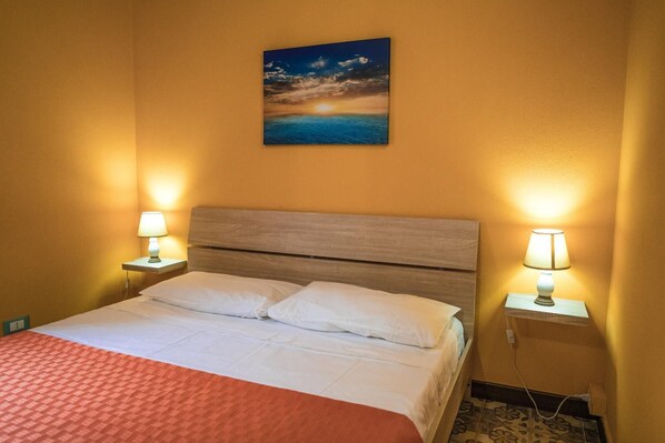 A hotel room with a bed, two bedside lamps, a painting of a sunset over water, and a red blanket. - Dream House 2  Castellamare del Golfo (Castellammare del golfo)