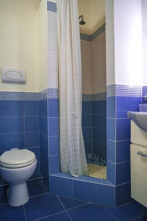 A bathroom with blue tiles, a toilet, a shower with a curtain, and a sink. - Dream House 2  Castellamare del Golfo (Castellammare del golfo)