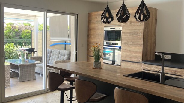 Cozinha moderna com bancada de madeira, banquetas pretas e luminárias pendentes.