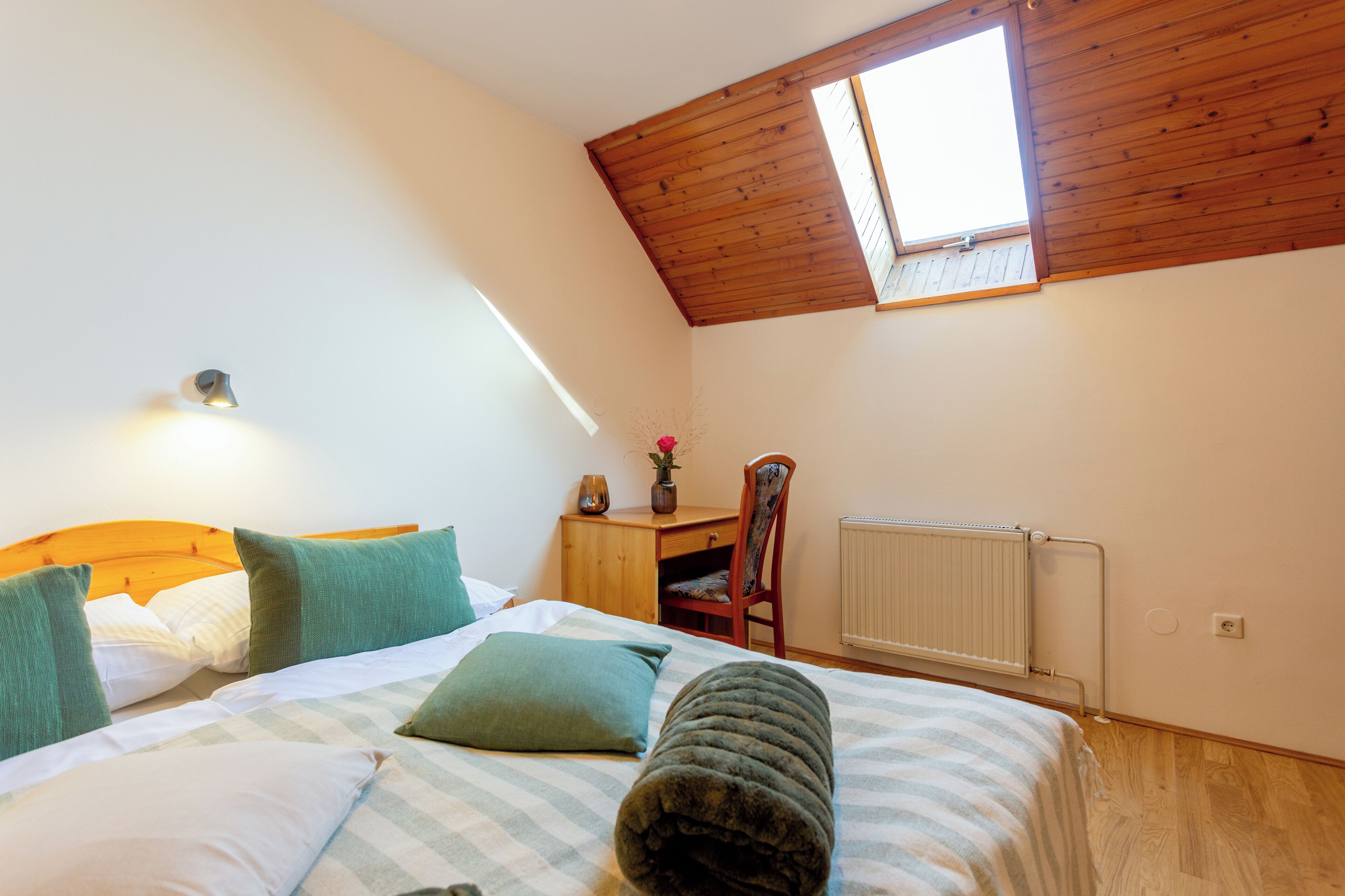 A bedroom with a bed, a desk, a chair, a radiator, and a skylight.