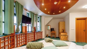 Een slaapkamer met een groot bed, groene gordijnen, een houten bureau, een televisie en een kledingkast.